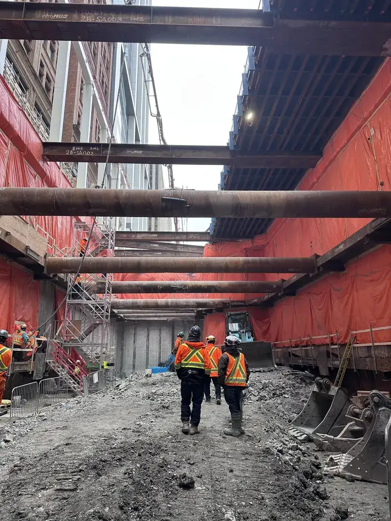 Braced excavation with construction crews and red perimeter sheeting